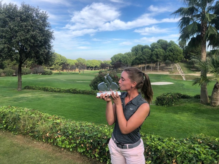 Laura Gómez, con el trofeo y el green del 18 al fondo. Foto: Santander Golf Tour.