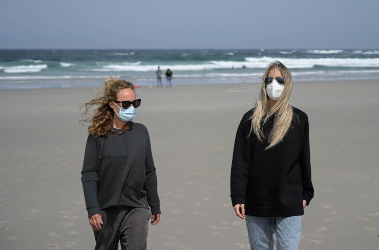 Dos chicas caminan por la playa con mascarilla