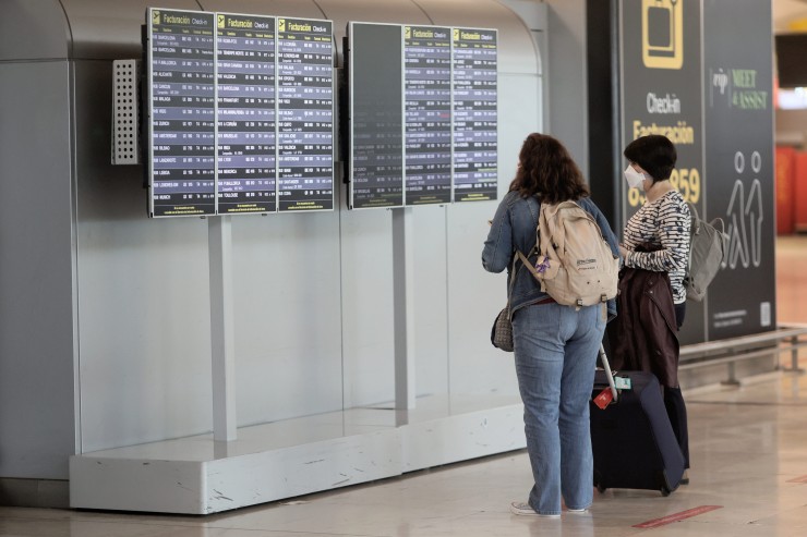 Dos pasajeras miran horarios de vuelo en un aeropuerto.