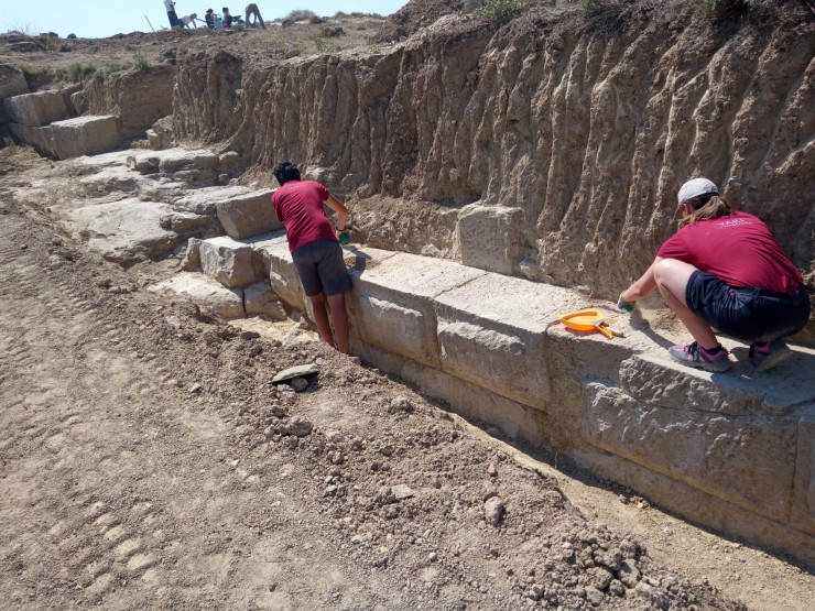 Dos estudiantes limpian los restos de lo que sería la muralla que cerraba la ciudad romana de Los Bañales