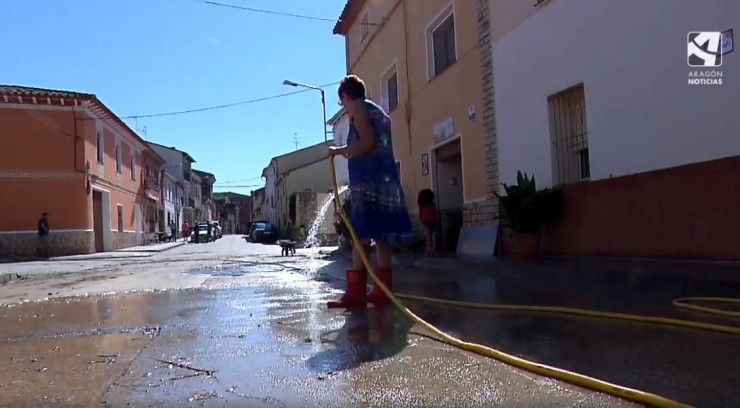 Una vecina de Sena limpia la calle con una manguera.