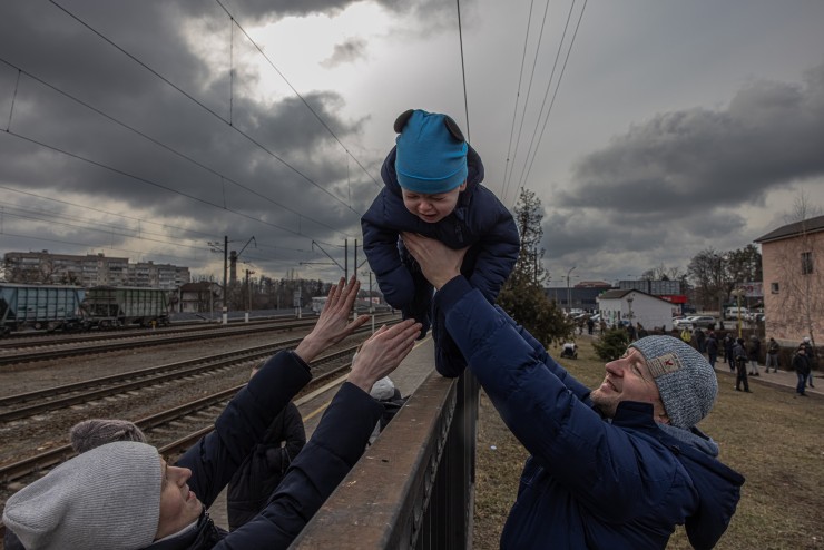 Un ciudadano ucraniano pasa por encima de una valla a su hijo antes de la llegada de un tren de evacuación. / Foto: EFE