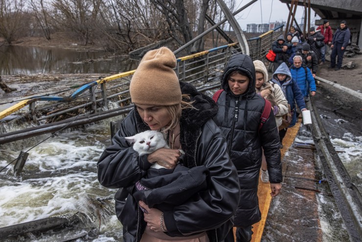 Una mujer con su gato cruza un puente destruido mientras los residentes huyen desde el frente de la ciudad de Irpín, en Kiev. / EFE