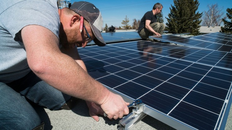 Dos operarios instalan placas solares en un edificio.