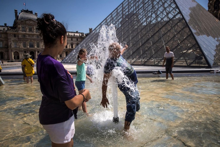 Un grupo de personas se refresca en una frente al Museo del Louvre, en París. / EFE