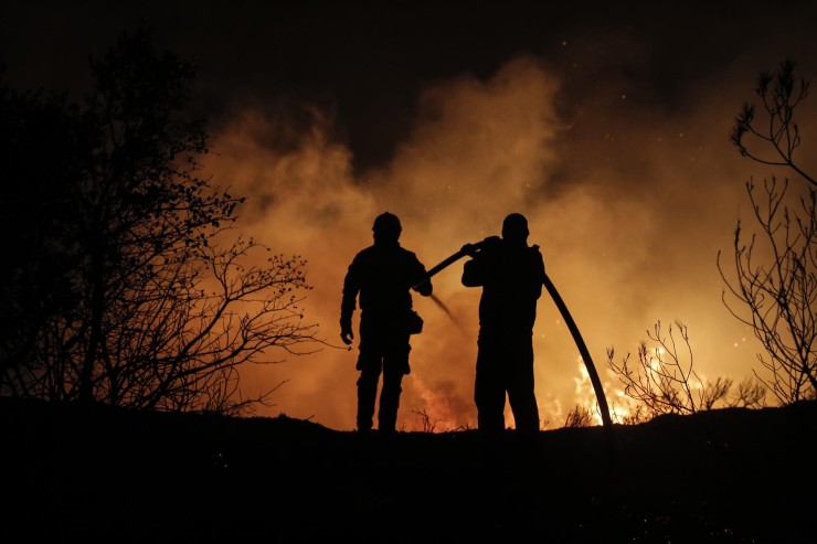 Dos bomberos tratan de reducir las llamas de uno de los incendios que está asolando Grecia. / EFE