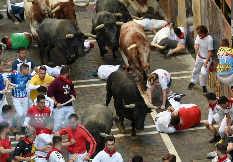 Los mozos corren y caen ante los toros de la ganadería de José Escolar durante el tercer del encierro de San Fermín, este sábado. (EFE/José Luis Larrión).