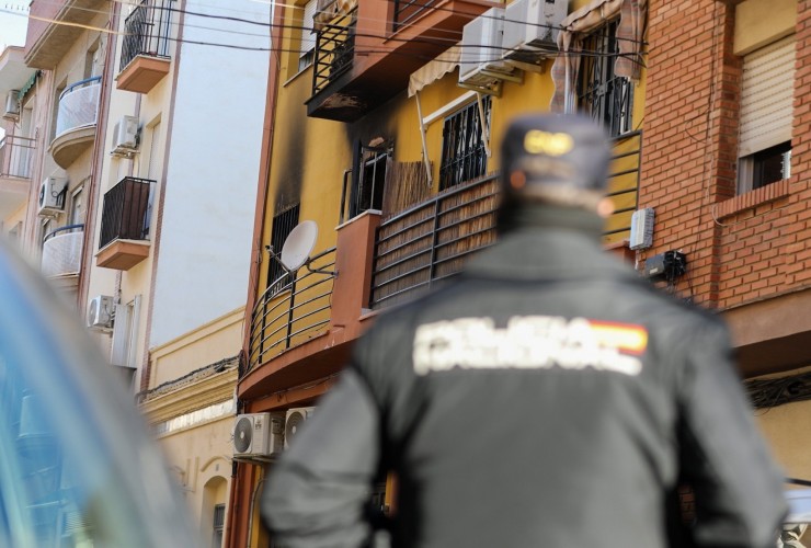 Un agende de Policía Nacional mira en dirección a la vivienda que ha sufrido el incendio en Huelva. / EP.