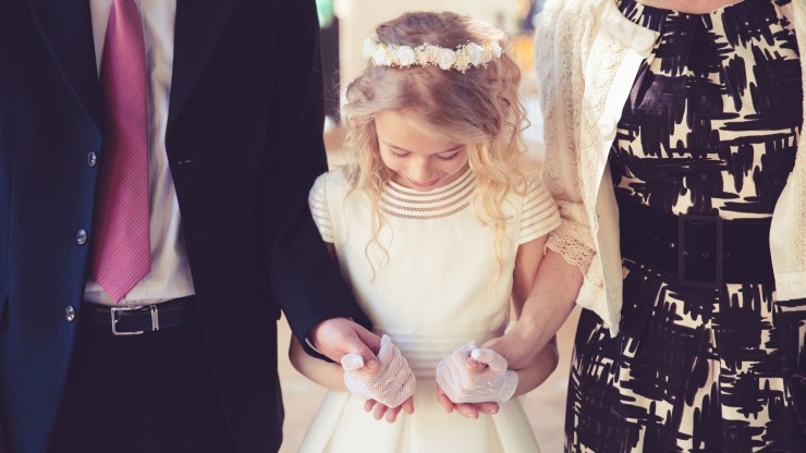 Una niña vestida de comunión junto a sus padres. / Canva.
