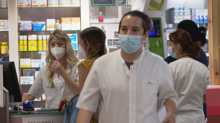 Trabajadores y clientes usando mascarilla en una farmacia.