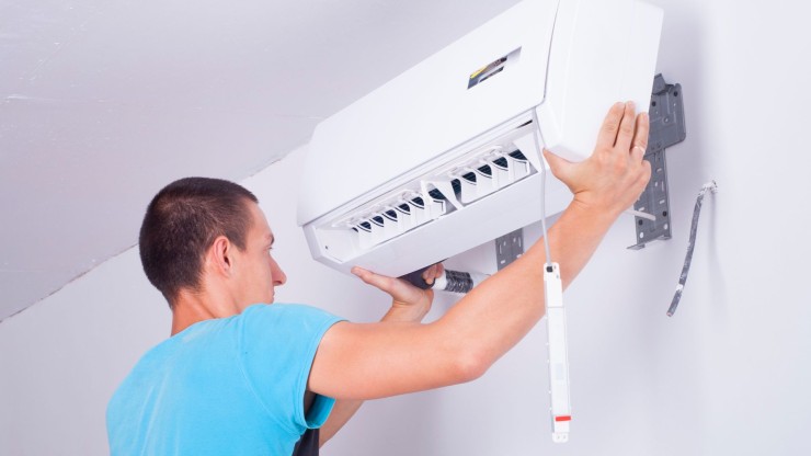 Un hombre instalando un aparato de aire acondicionado. / Canva.