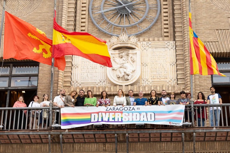 Miembros de la ejecutiva municipal y de la oposición colocan la bandera LGTBIQ+ en el balcón del Ayuntamiento de Zaragoza junto a parte del colectivo.